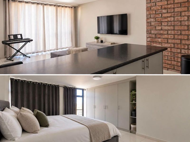 A modern open-plan living area featuring a kitchen island, exposed brick wall, and a bedroom with extensive built-in cabinetry and neutral finishes.