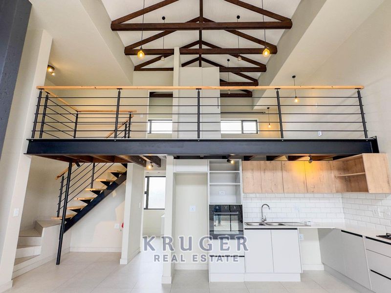 Modern open-plan living area featuring a mezzanine level, exposed timber trusses, and a contemporary kitchen with built-in appliances and sleek cabinetry.