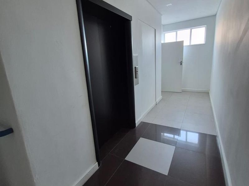 A clean, modern office hallway featuring tiled flooring, recessed lighting, and direct access to an elevator.