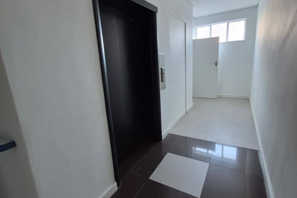 A clean, modern office hallway featuring tiled flooring, recessed lighting, and direct access to an elevator.