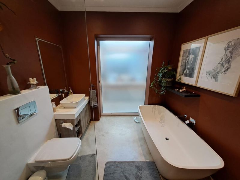 Modern bathroom featuring a freestanding bathtub, wall-mounted toilet, vessel sink vanity, and a large frosted glass window providing natural light.