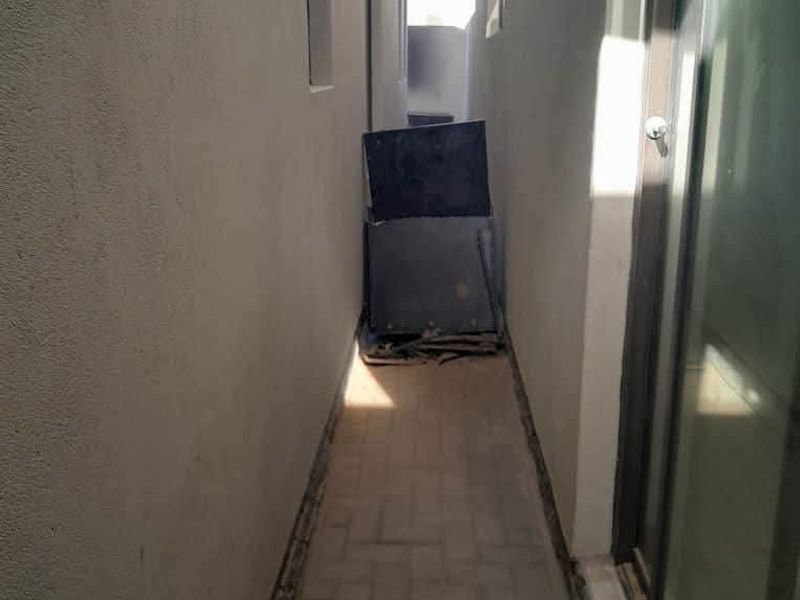 A narrow side passage or exterior walkway featuring paved flooring and access to the home via a sliding glass door.