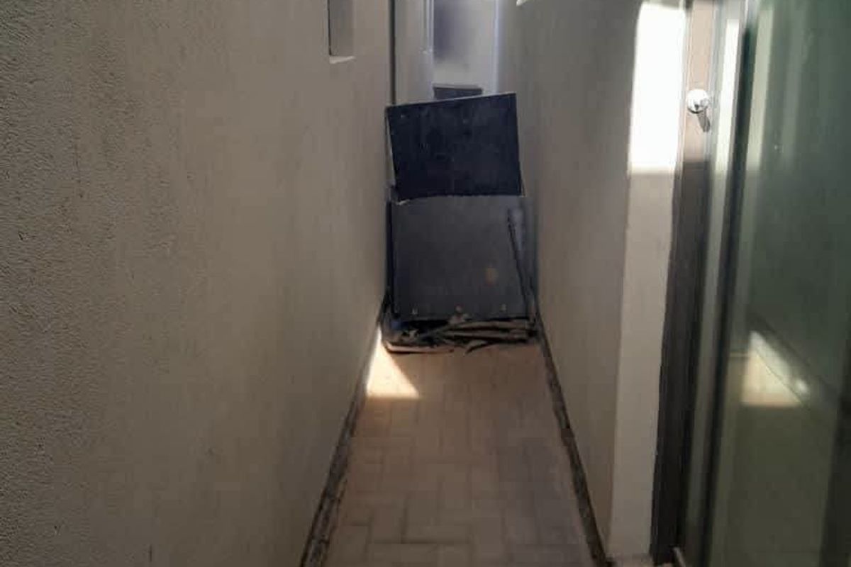A narrow side passage or exterior walkway featuring paved flooring and access to the home via a sliding glass door.