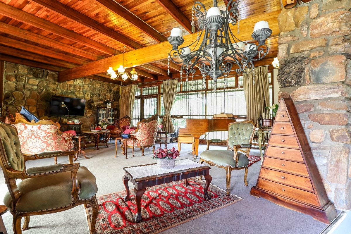 Spacious living room featuring a rustic stone wall, exposed timber beam ceiling, and a large decorative chandelier, creating a warm and traditional atmosphere.