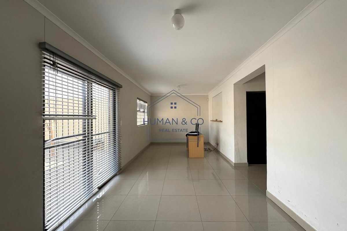A spacious, empty living area featuring neutral tiled flooring, large sliding glass doors with venetian blinds, and clean white walls.