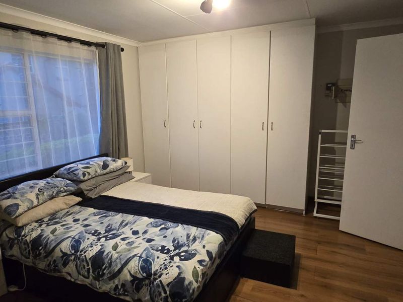 A well-maintained bedroom featuring laminate flooring and extensive floor-to-ceiling built-in cupboards, providing ample storage space.