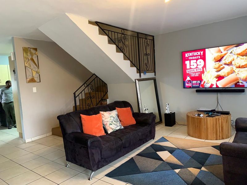 A living room featuring ceramic floor tiles and an open staircase with a decorative wrought iron balustrade.