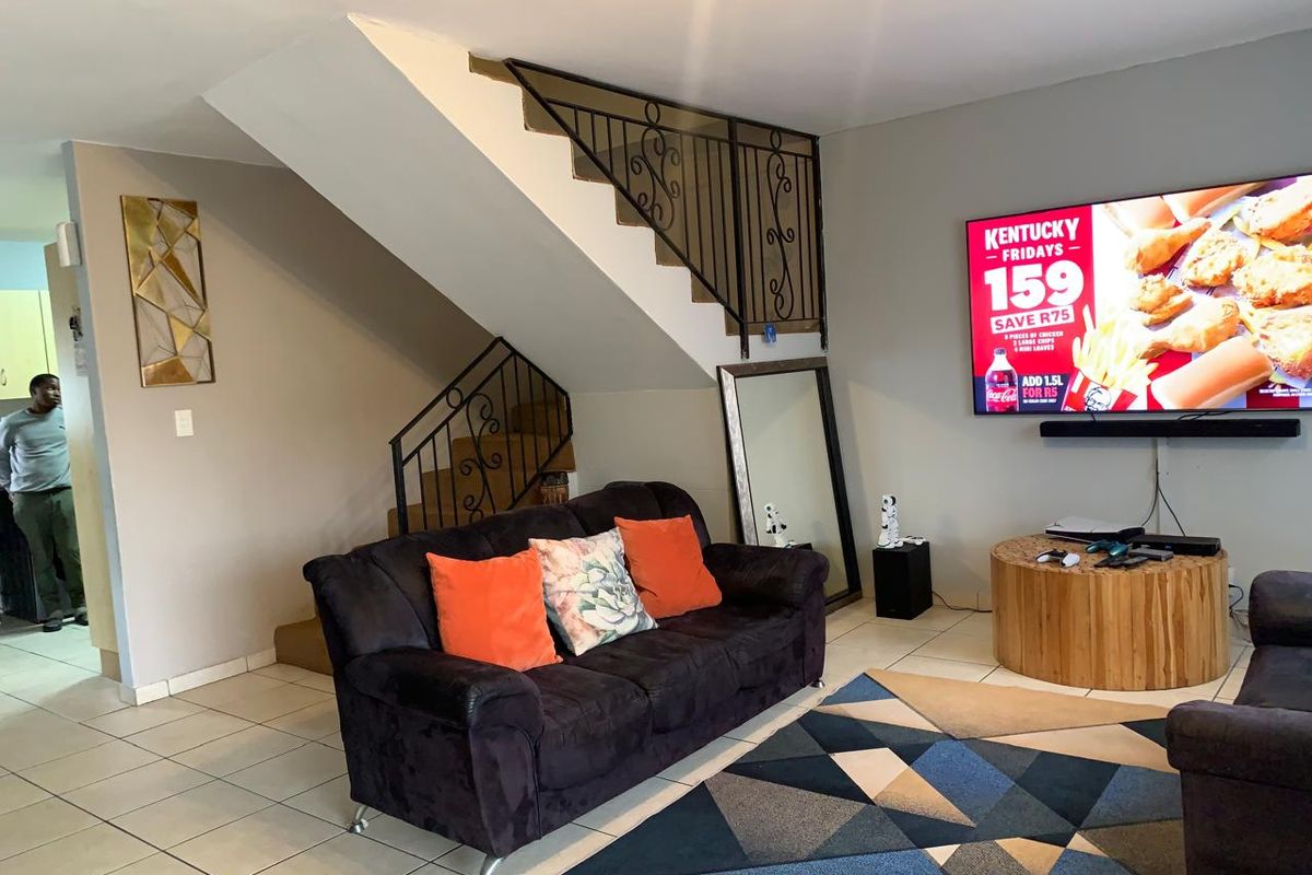 A living room featuring ceramic floor tiles and an open staircase with a decorative wrought iron balustrade.