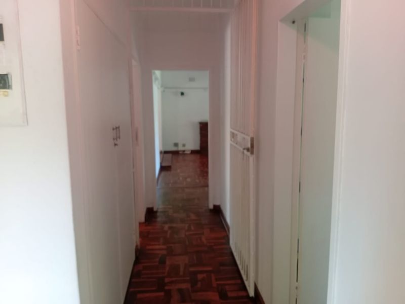 A functional hallway featuring classic parquet flooring, a security gate, and built-in storage cupboards, providing access to other areas of the home.