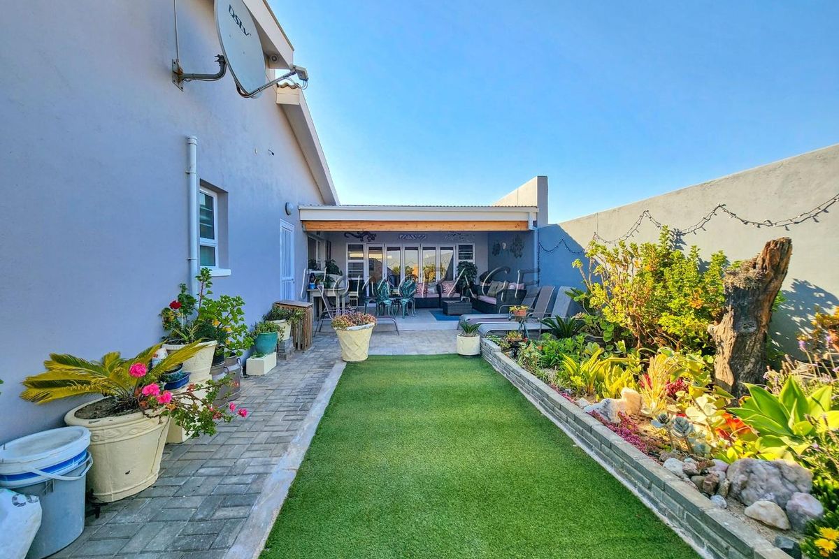 A well-maintained rear garden featuring an artificial lawn, raised garden beds, and a covered patio area accessible through glass sliding doors.