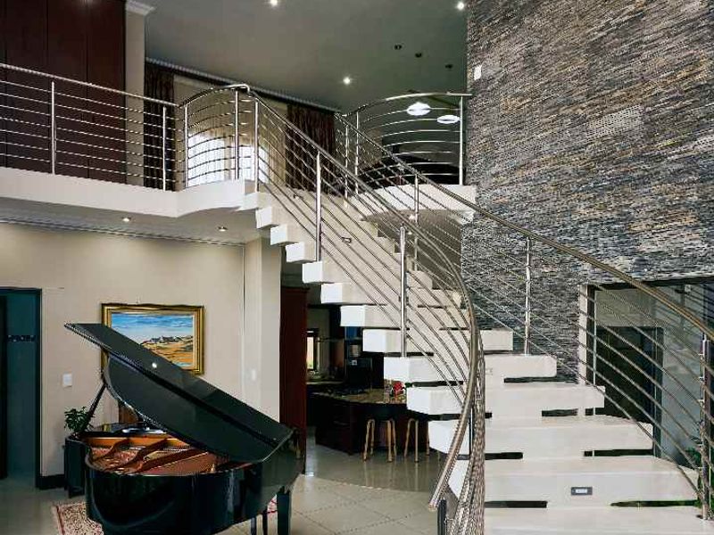 Grand double-volume living area featuring a striking floating staircase with stainless steel balustrades, a textured stone feature wall, and an elegant crystal chandelier.