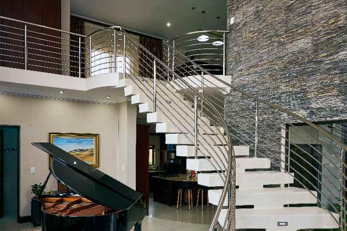 Grand double-volume living area featuring a striking floating staircase with stainless steel balustrades, a textured stone feature wall, and an elegant crystal chandelier.