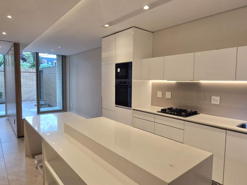 Modern, high-end kitchen featuring sleek handleless cabinetry, stone countertops, integrated appliances, and recessed lighting, leading out to a private courtyard area.