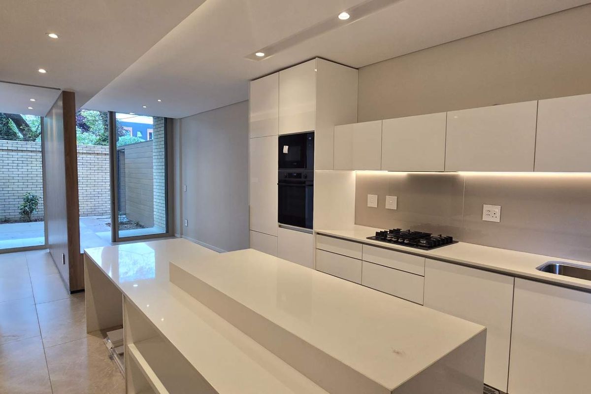 Modern, high-end kitchen featuring sleek handleless cabinetry, stone countertops, integrated appliances, and recessed lighting, leading out to a private courtyard area.