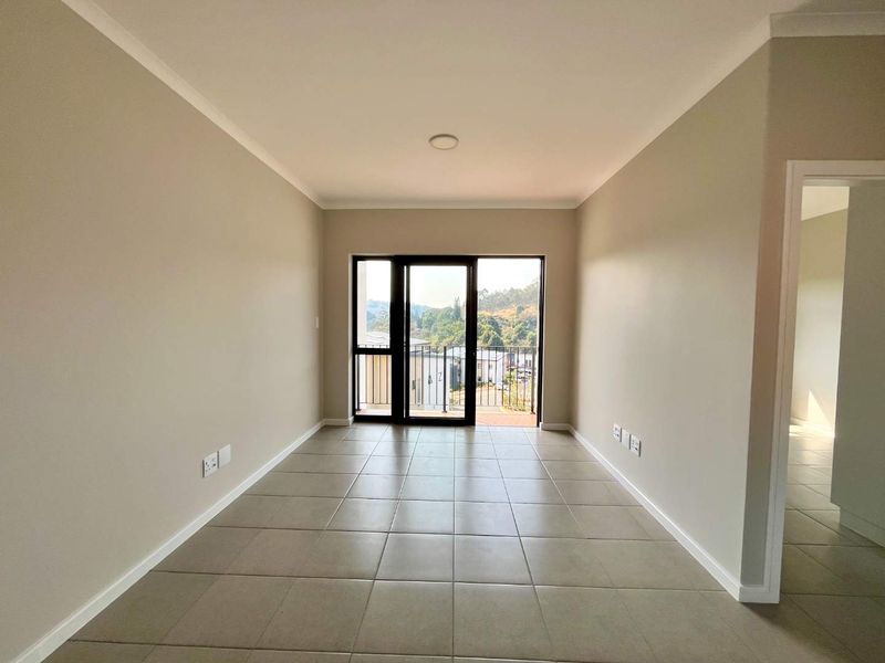 A bright, empty living area featuring neutral walls, tiled flooring, and a sliding glass door providing access to a balcony with scenic views.