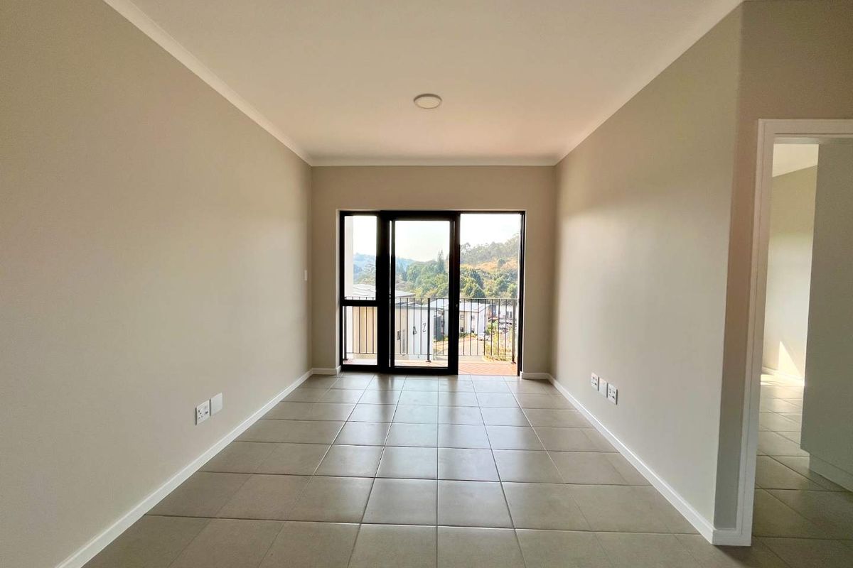 A bright, empty living area featuring neutral walls, tiled flooring, and a sliding glass door providing access to a balcony with scenic views.