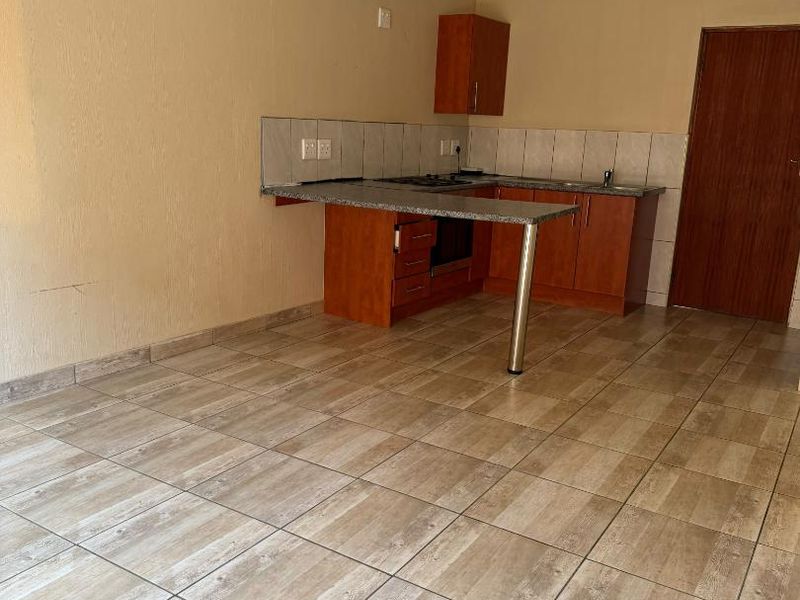 An empty kitchen featuring wooden cabinetry, granite countertops, a built-in oven and hob, and neutral tiled flooring.