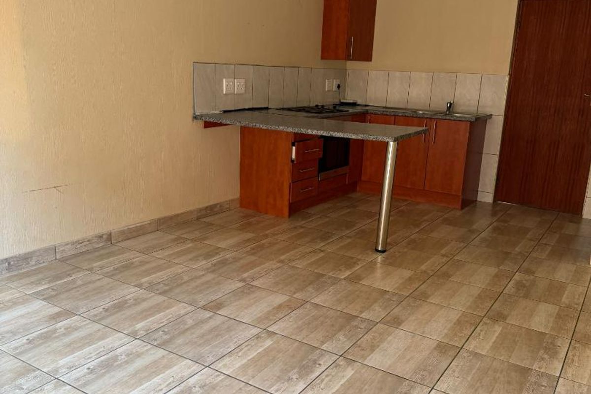An empty kitchen featuring wooden cabinetry, granite countertops, a built-in oven and hob, and neutral tiled flooring.