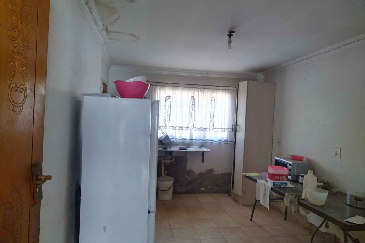 A kitchen space requiring significant renovation, featuring visible water damage on the ceiling and wall surfaces, with basic tiled flooring and sink installation.