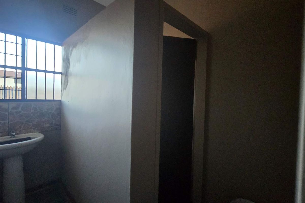 A basic bathroom featuring a pedestal basin, security bars on the window, and a partitioned toilet area.