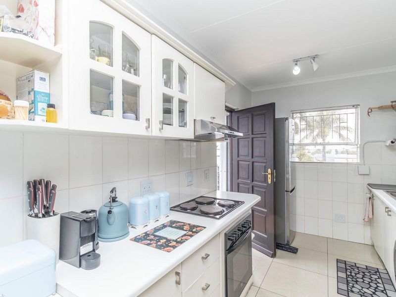 A functional kitchen featuring white cabinetry, built-in electric hob and oven, extractor fan, tiled splashbacks, and tiled flooring.