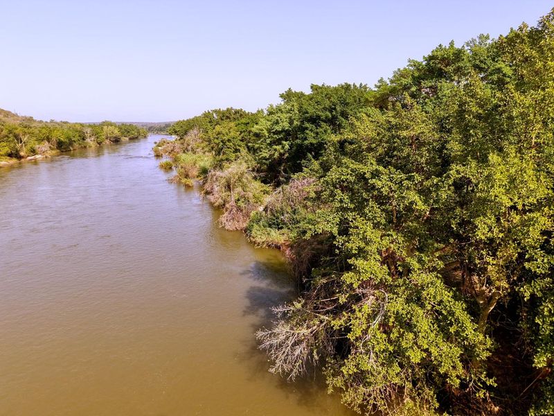 A scenic view of a river flowing alongside a lush, tree-lined bank, showcasing the natural beauty and tranquil setting of the property.
