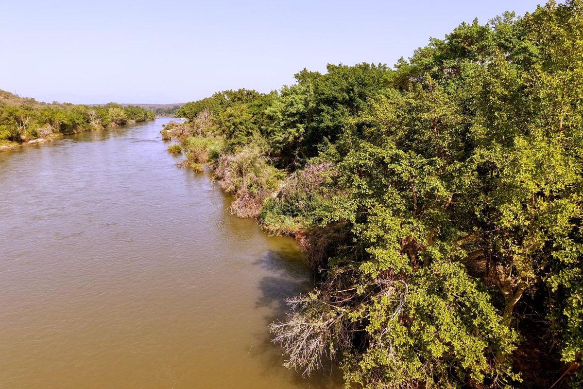 A scenic view of a river flowing alongside a lush, tree-lined bank, showcasing the natural beauty and tranquil setting of the property.