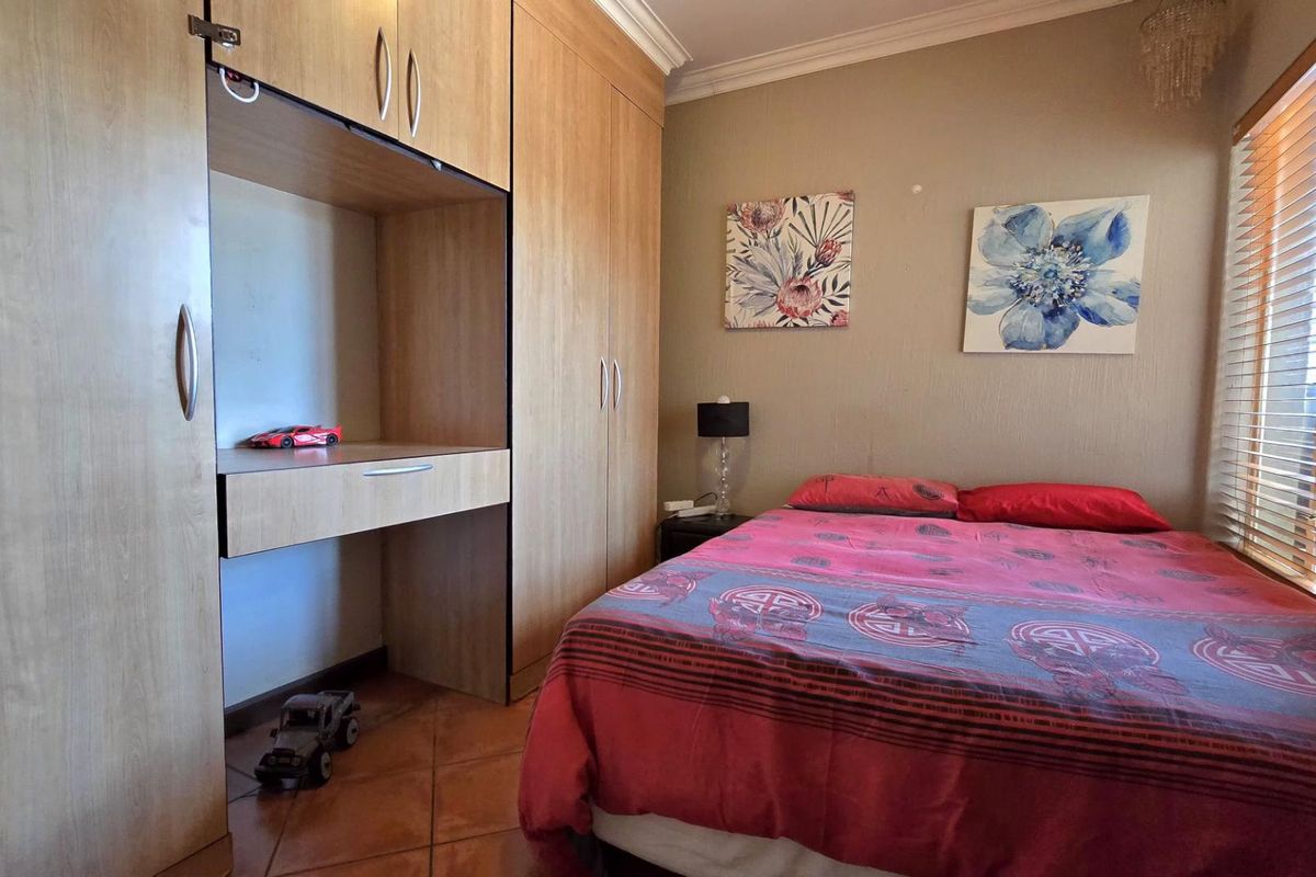 A bedroom featuring built-in wooden cupboards with an integrated desk, tiled flooring, and venetian blinds.