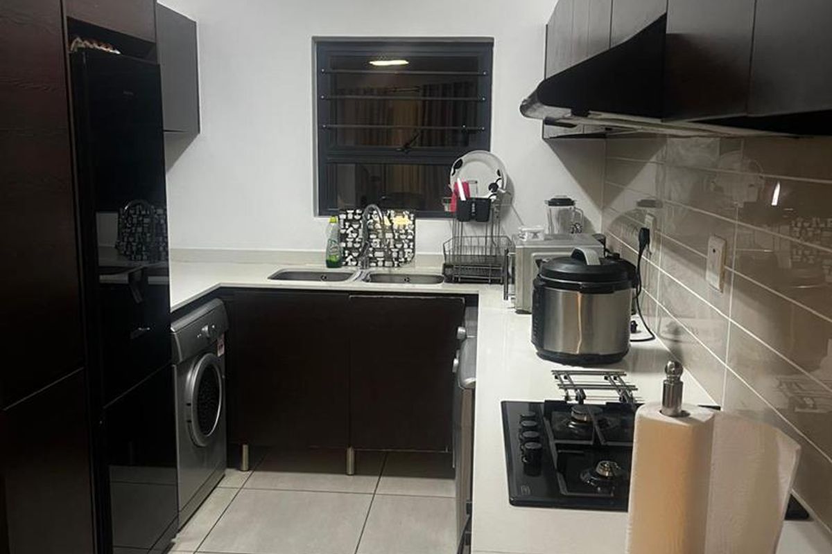 Modern kitchen featuring dark cabinetry, light stone countertops, tiled flooring, integrated gas hob, and built-in laundry appliance space.