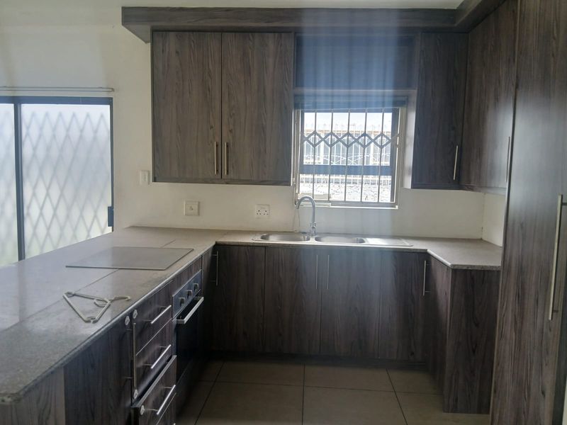 A functional kitchen featuring dark wood-grain cabinetry, laminate countertops, built-in oven and hob, and a double sink with a security-barred window.
