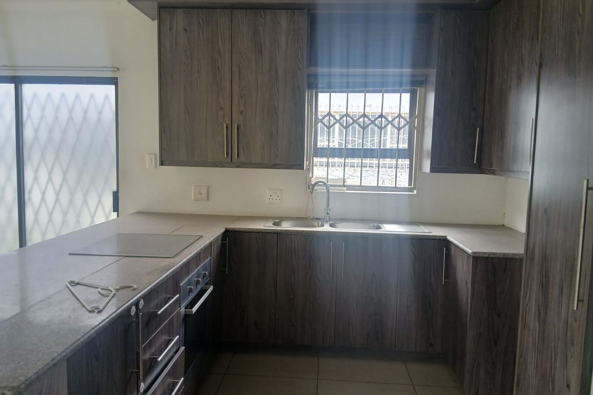 A functional kitchen featuring dark wood-grain cabinetry, laminate countertops, built-in oven and hob, and a double sink with a security-barred window.