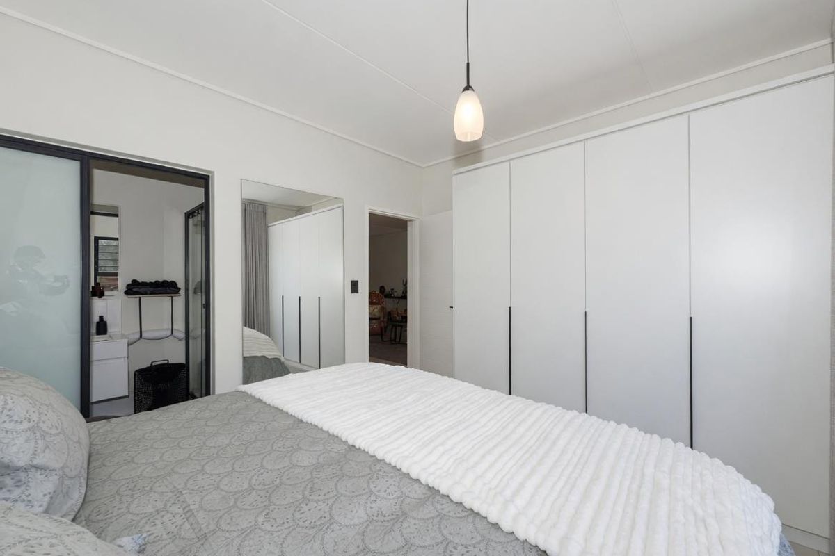 A well-maintained bedroom featuring extensive built-in floor-to-ceiling wardrobes, a modern pendant light, and an en-suite bathroom with a glass door entry.