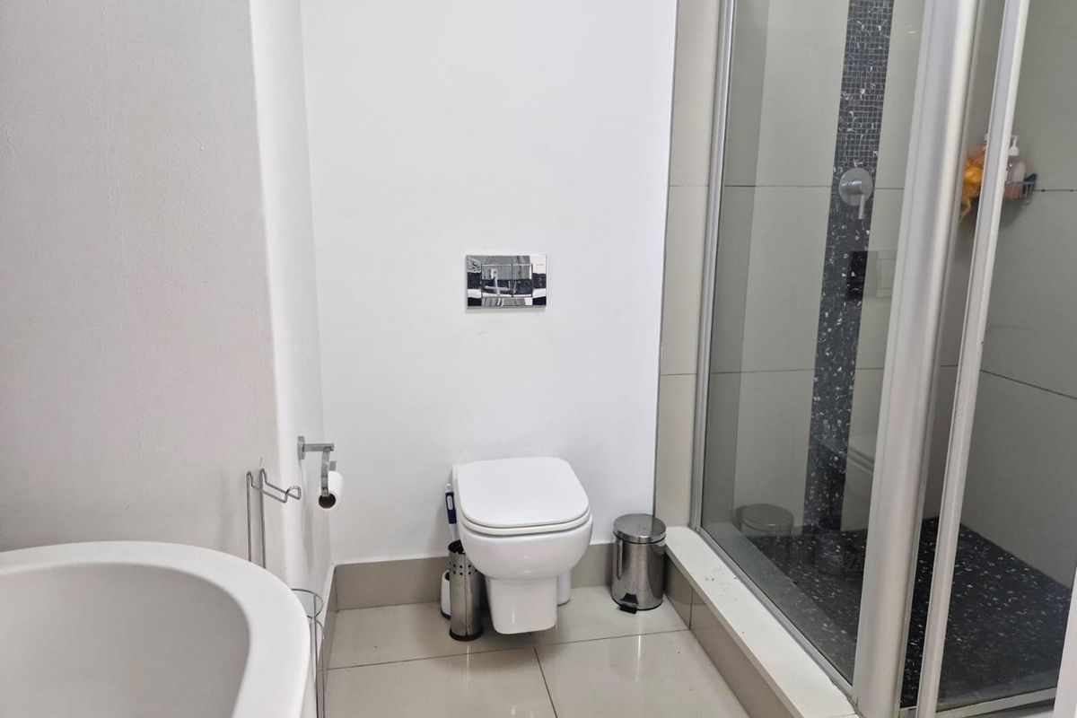 Modern bathroom featuring a wall-mounted toilet, a glass-enclosed shower with mosaic tile accents, and neutral floor tiling.