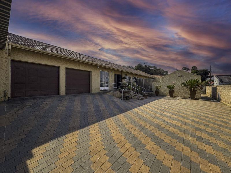 Front exterior view of the property featuring a spacious paved driveway, double garage, and accessible entrance with metal handrails.