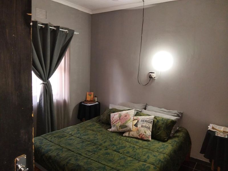 A cozy bedroom featuring neutral grey walls, a wall-mounted light fixture, and a window with curtain treatments.