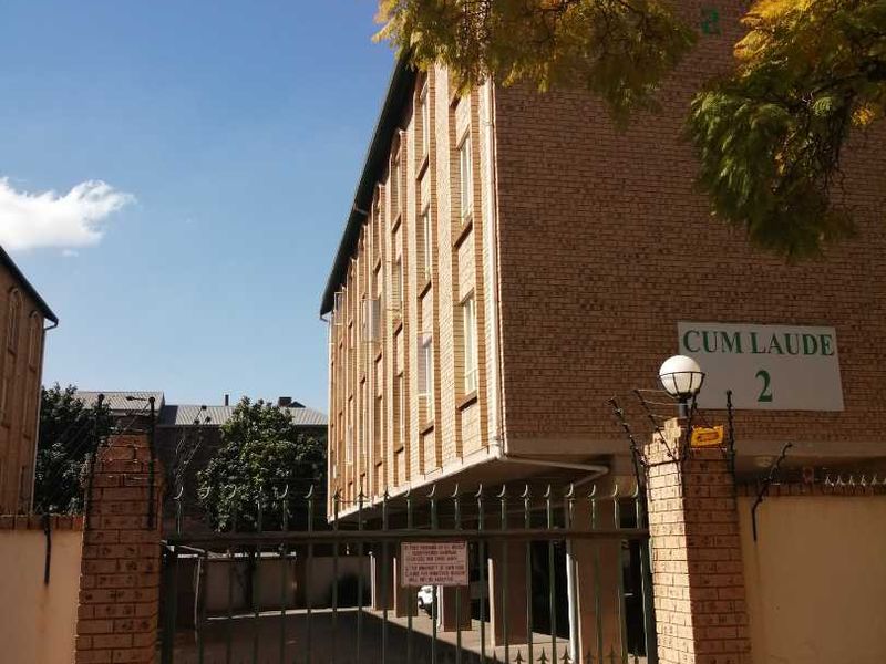 Exterior view of the Cum Laude apartment complex featuring a brick facade, secure gated entrance, and paved driveway access.
