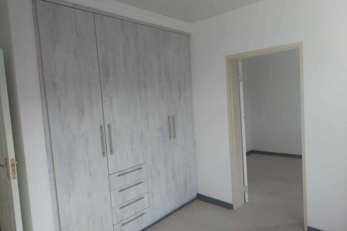 A bright bedroom featuring built-in cupboards with a light wood-grain finish and a doorway leading to an adjacent room.