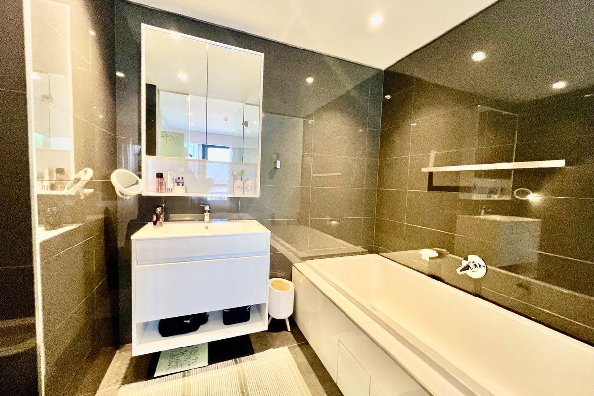Modern bathroom featuring dark tiled walls, a white built-in vanity with integrated storage, a mirrored medicine cabinet, and a clean bathtub.