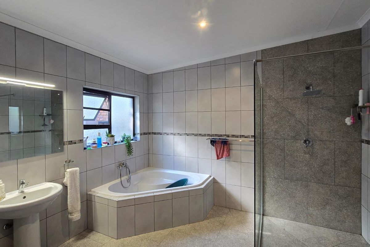 A well-maintained bathroom featuring a corner bathtub, a separate glass-enclosed shower, and a pedestal basin with neutral wall and floor tiling.