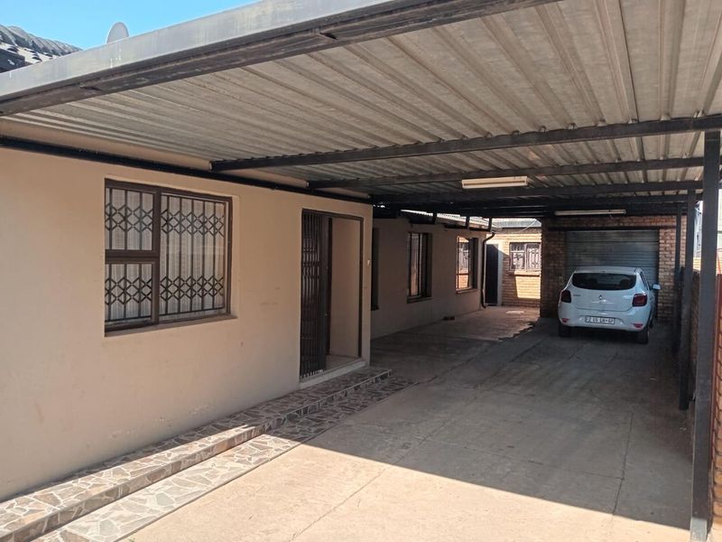Front exterior view featuring a covered carport, concrete driveway, and security gates providing access to the main entrance.