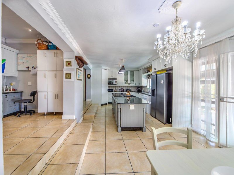 Spacious open-plan kitchen featuring a central island with granite countertops, ample built-in cabinetry, and tiled flooring, seamlessly connected to a functional workspace area.
