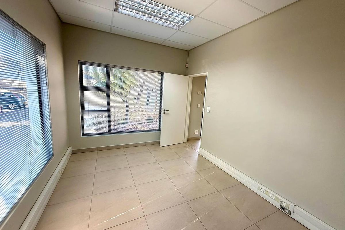 A clean, empty office space featuring tiled flooring, recessed ceiling lighting, and large windows with fitted blinds, suitable for a professional workspace.