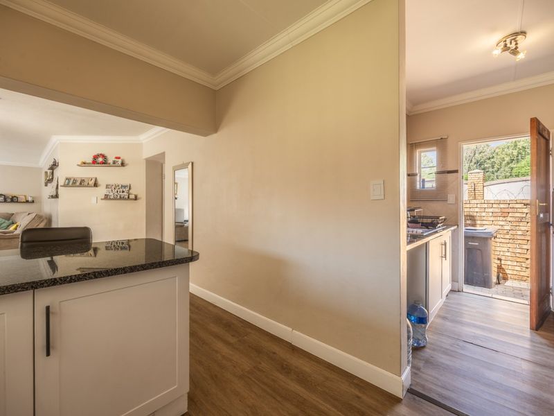 Open plan living area featuring laminate flooring, crown molding, and a kitchen with granite countertops, leading to an exterior rear access point.