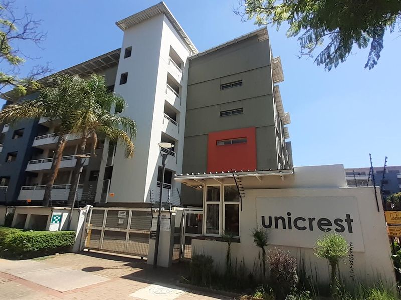 Front exterior view of the Unicrest apartment complex featuring a secure gated entrance, perimeter wall with electric fencing, and a dedicated guard house.