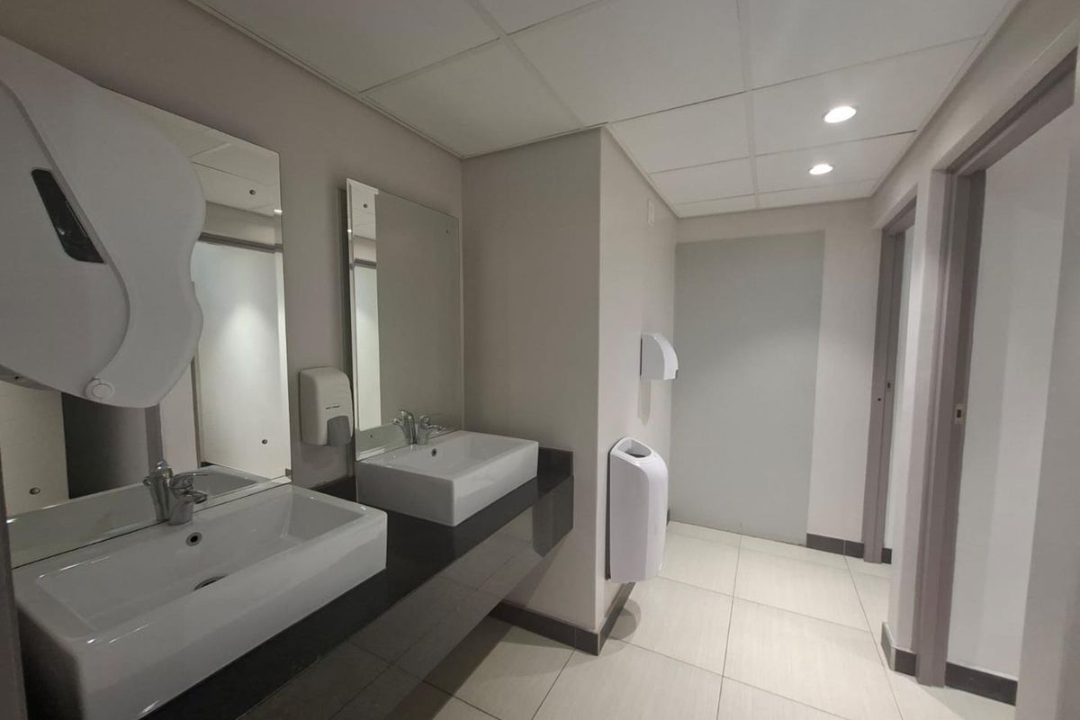 A clean, modern office restroom featuring dual vessel sinks, a dark vanity countertop, tiled flooring, and recessed ceiling lighting.
