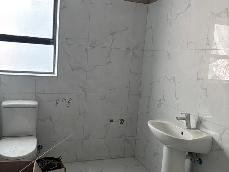 A bathroom in the final stages of renovation featuring marble-look tiling, a pedestal basin, and a toilet, requiring final plastering and finishing touches.