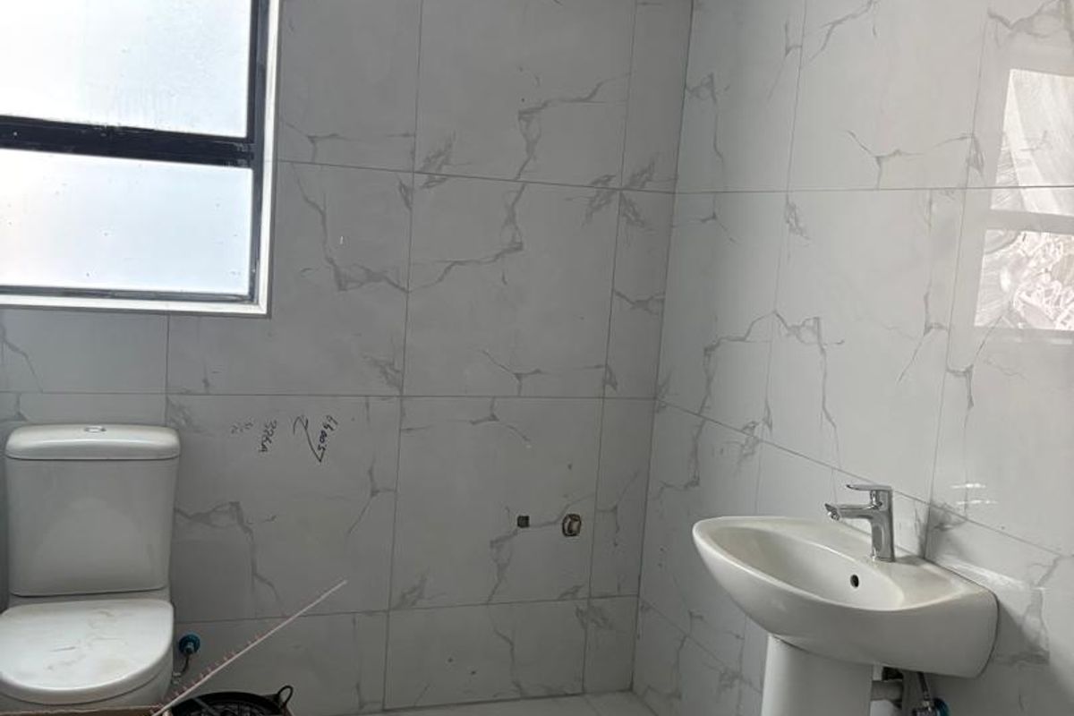 A bathroom in the final stages of renovation featuring marble-look tiling, a pedestal basin, and a toilet, requiring final plastering and finishing touches.