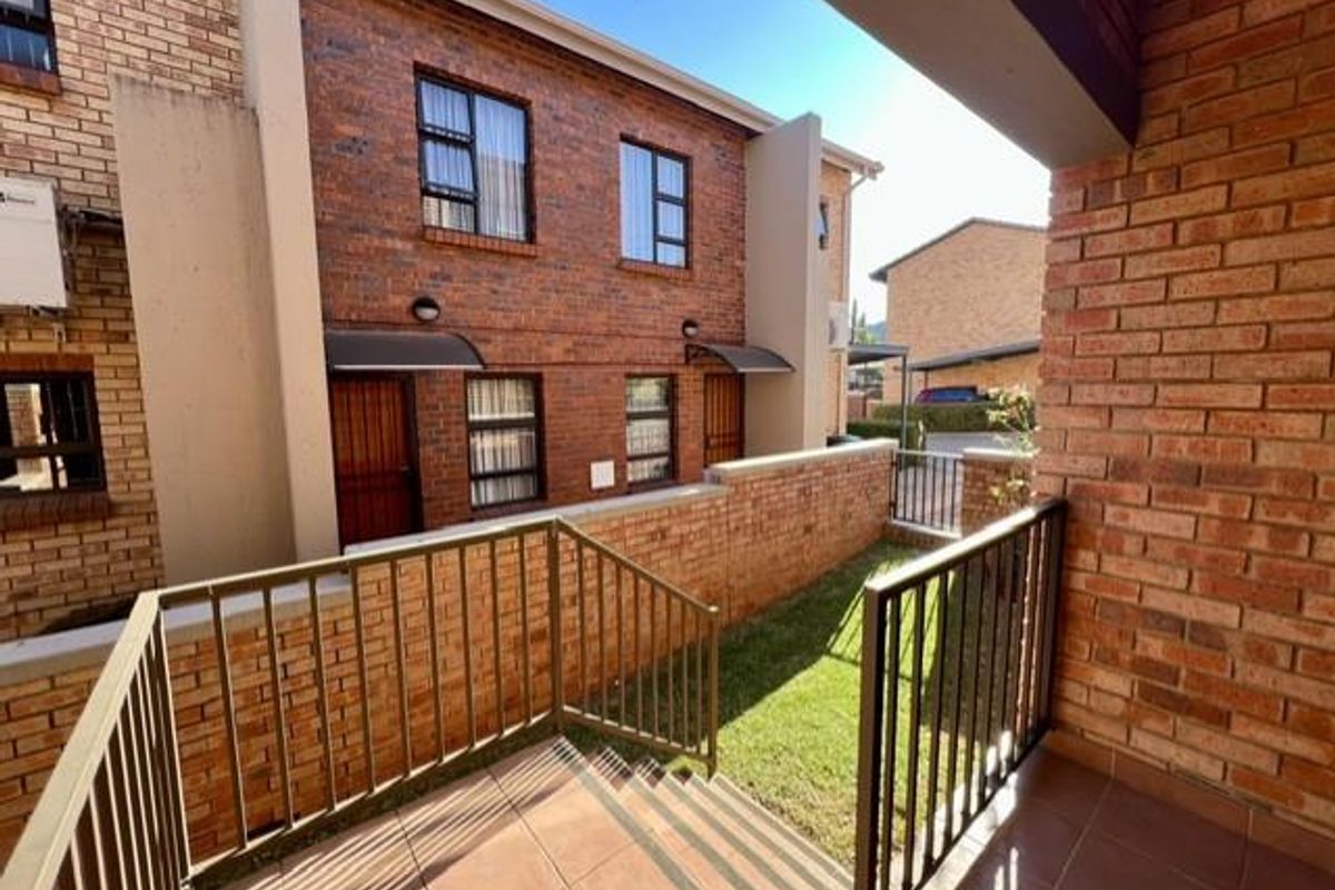 A rear view of a face brick townhouse featuring a tiled patio, metal balustrades, and a small private garden area.