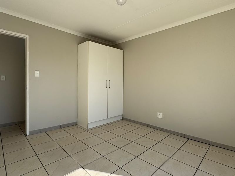 A clean, empty bedroom featuring neutral wall paint, tiled flooring, and a built-in wardrobe, offering a blank canvas for personalization.