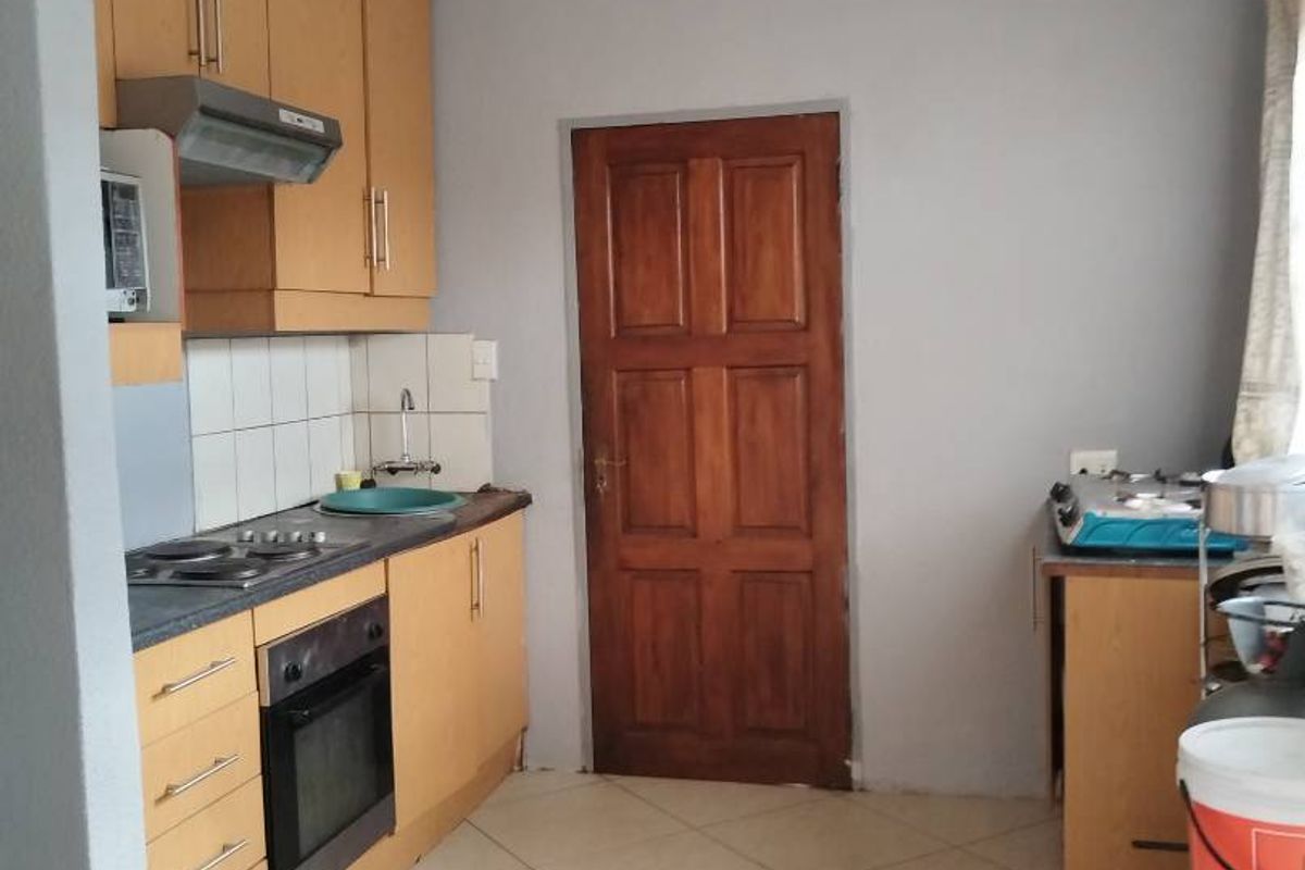 A functional kitchen featuring light wood cabinetry, built-in oven and hob, tiled backsplash, and neutral floor tiles with a solid wood door.